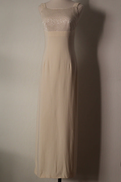 A sleeveless cream-colored maxi dress with a sheer lace bodice and a solid satin-like skirt, displayed on a mannequin against a plain wall.