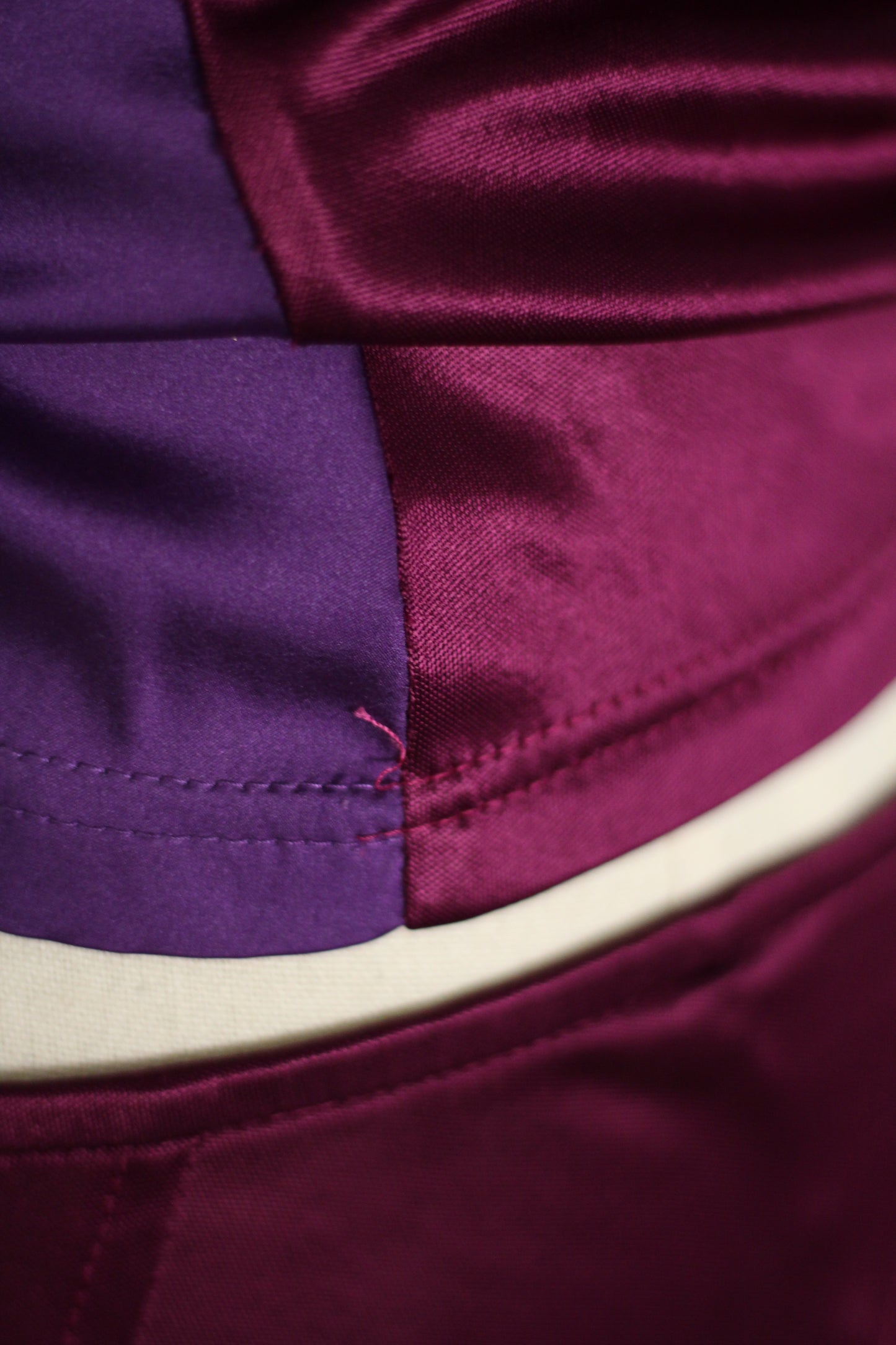 Close-up of a satin garment with a color-blocked design in deep purple and burgundy, featuring a curved cream-colored waistband.