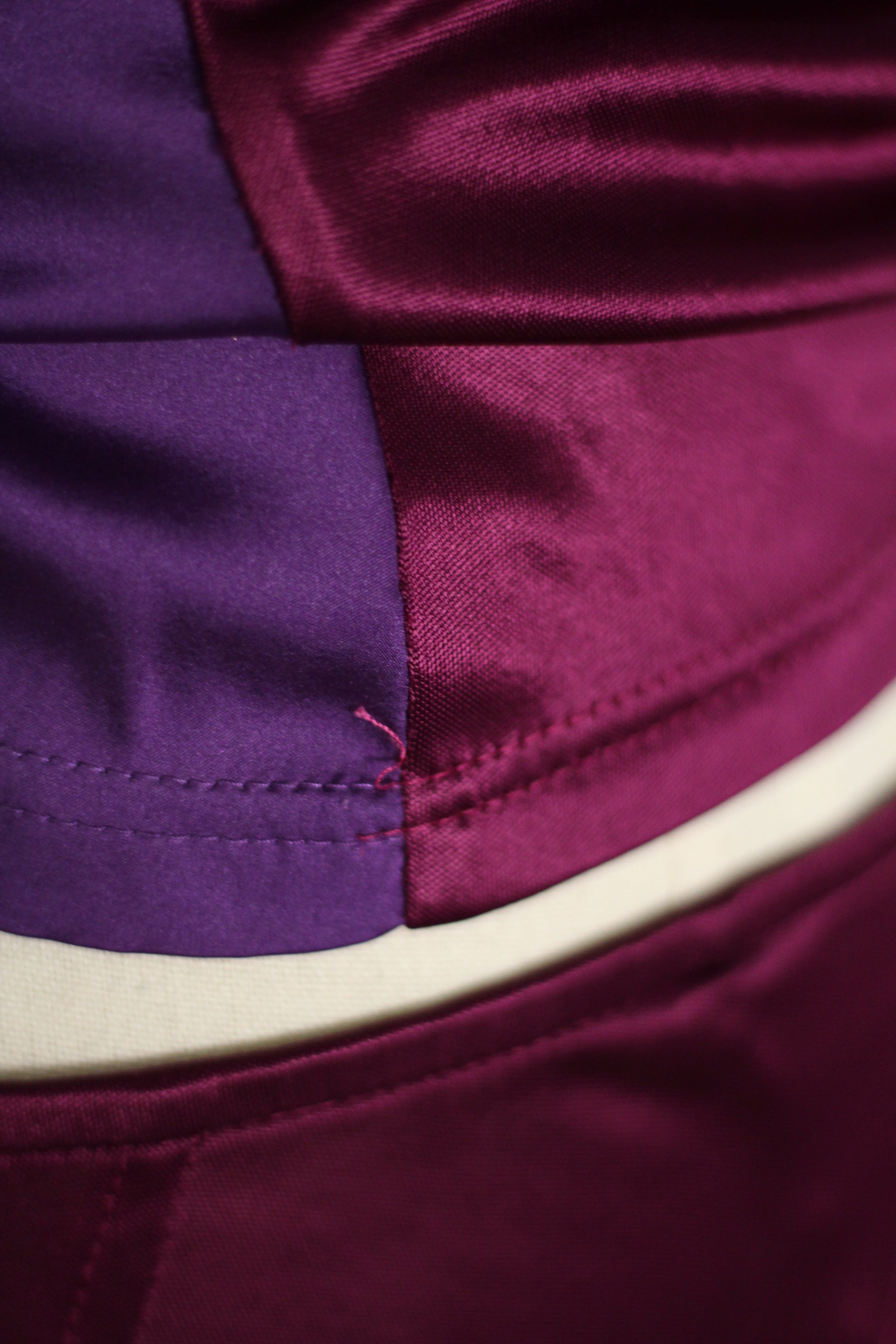 Close-up of a satin garment with a color-blocked design in deep purple and burgundy, featuring a curved cream-colored waistband.