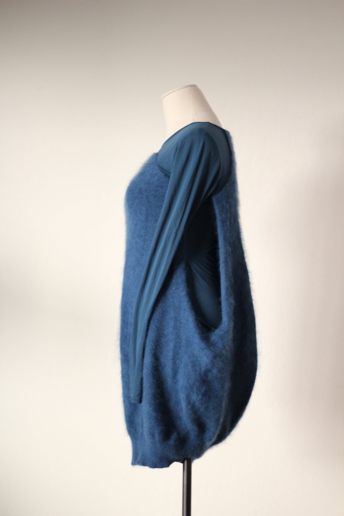 Side profile of Alexander McQueen Fall/Winter 2007 blue angora sweater dress featuring a long fitted sleeve, textured angora exterior, open side revealing the inner dress, and rounded cocoon silhouette.