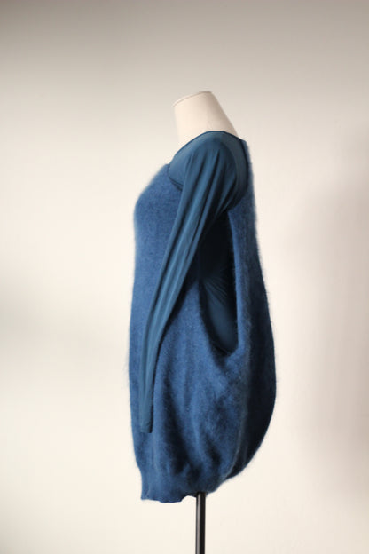 Side profile of Alexander McQueen Fall/Winter 2007 blue angora sweater dress featuring a long fitted sleeve, textured angora exterior, open side revealing the inner dress, and rounded cocoon silhouette.