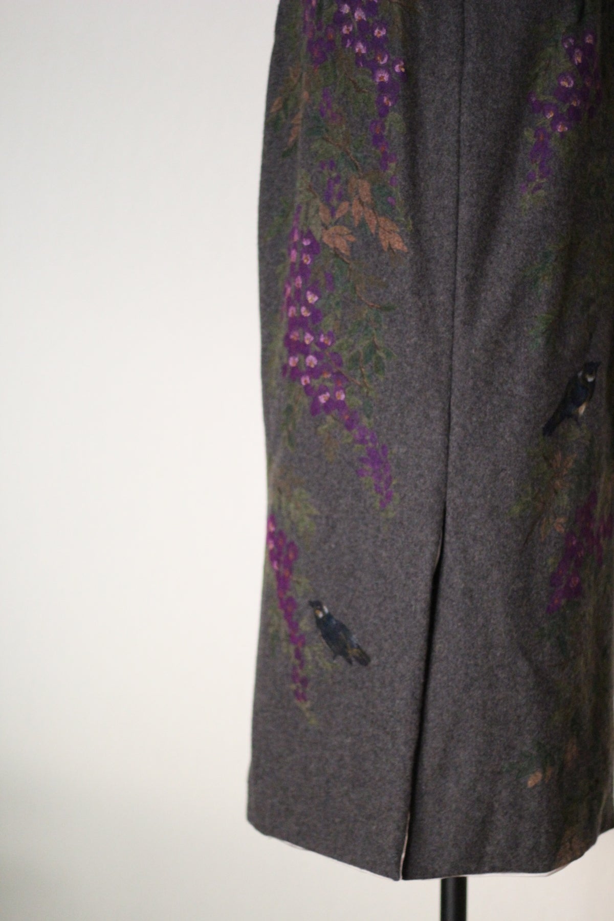 Close-up of the back of a vintage Dolce & Gabbana Fall/Winter 1998 runway dress featuring hand-painted purple wisteria flowers, blue birds, and a center back slit on gray wool fabric.