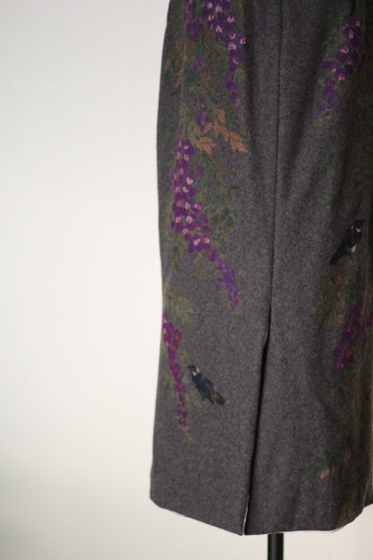 Close-up of the back of a vintage Dolce & Gabbana Fall/Winter 1998 runway dress featuring hand-painted purple wisteria flowers, blue birds, and a center back slit on gray wool fabric.