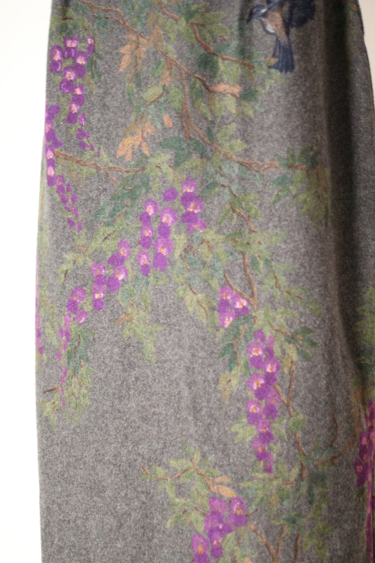 Close-up of vintage Dolce & Gabbana Fall/Winter 1998 runway dress featuring hand-painted purple wisteria flowers, green leaves, delicate branches, and a partial blue bird motif on gray wool fabric.