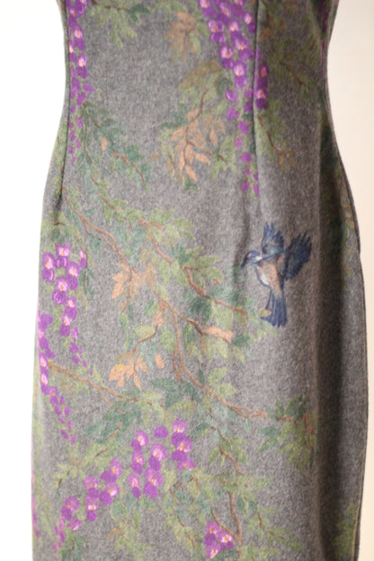 Close-up of vintage Dolce & Gabbana Fall/Winter 1998 runway dress showing a painted blue bird surrounded by purple wisteria flowers, green foliage, and branches on gray wool fabric.