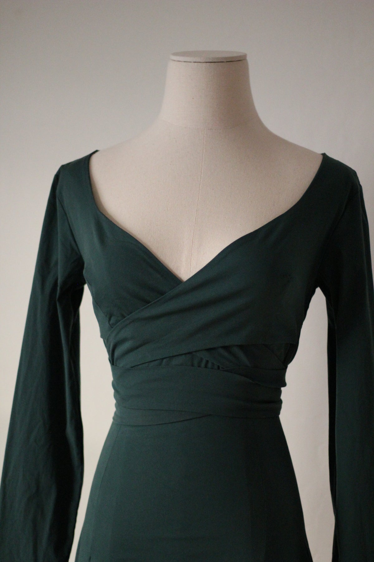 Close-up of a dark green wrap dress showing the deep V-neckline, overlapping bodice, long sleeves, and fitted waist