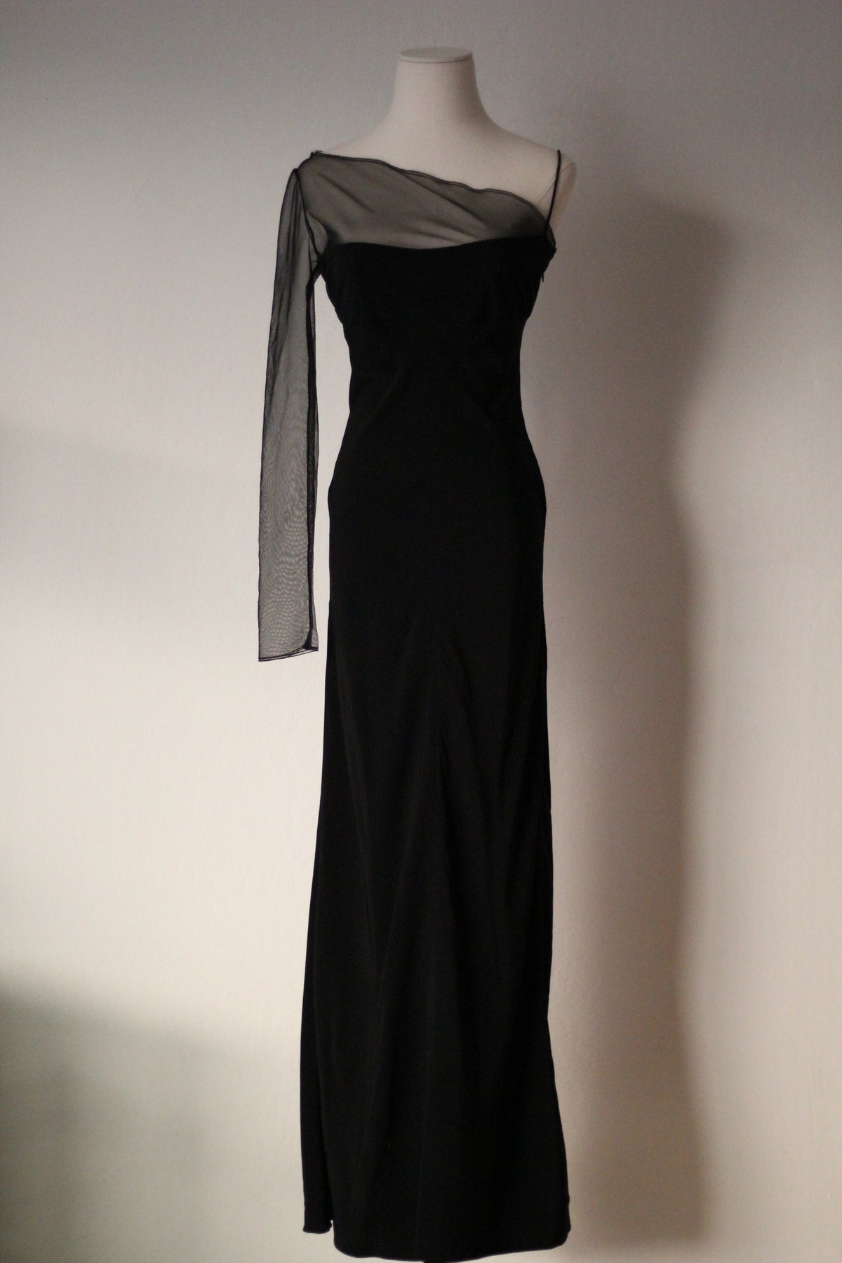 Black Richard Tyler Spring/Summer 1997 floor-length gown with an asymmetrical neckline, sheer mesh sleeve, and fitted silhouette, shown from an angled view