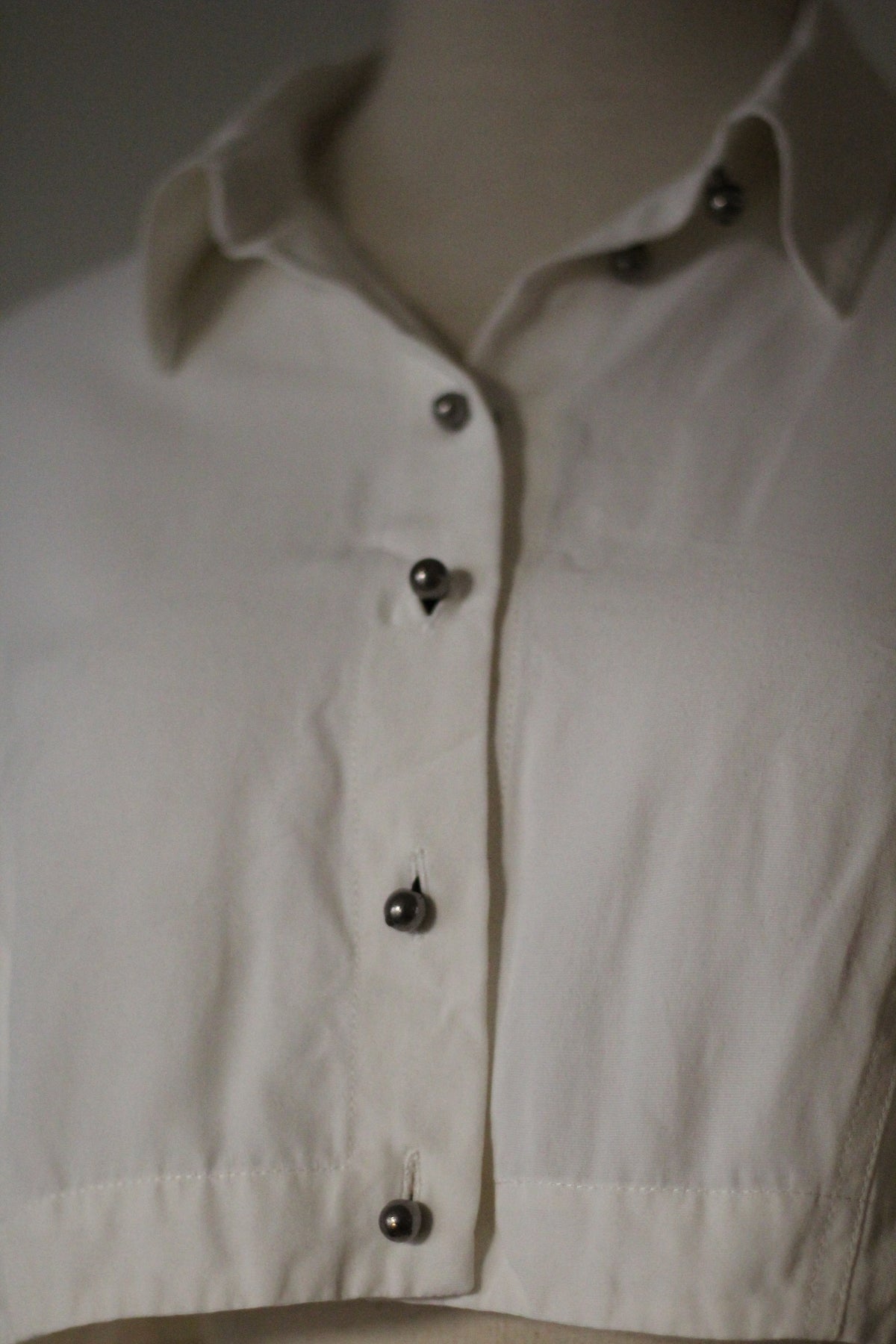 Close-up of the Rifat Ozbek Spring/Summer 1994 white cropped shirt featuring a pointed collar and dark button-front detailing.