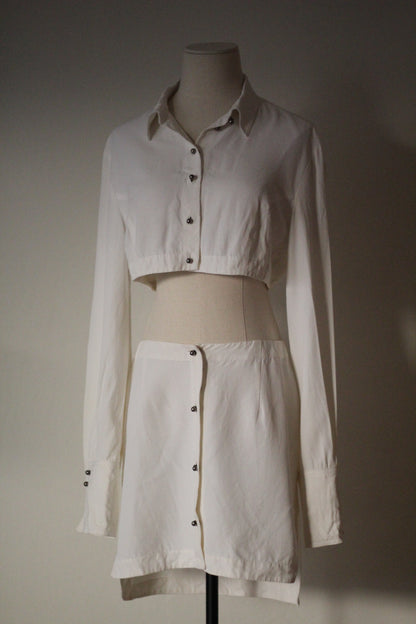 Front view of a Rifat Ozbek Spring/Summer 1994 white matching set featuring a cropped button-front shirt and high-waisted mini skirt.