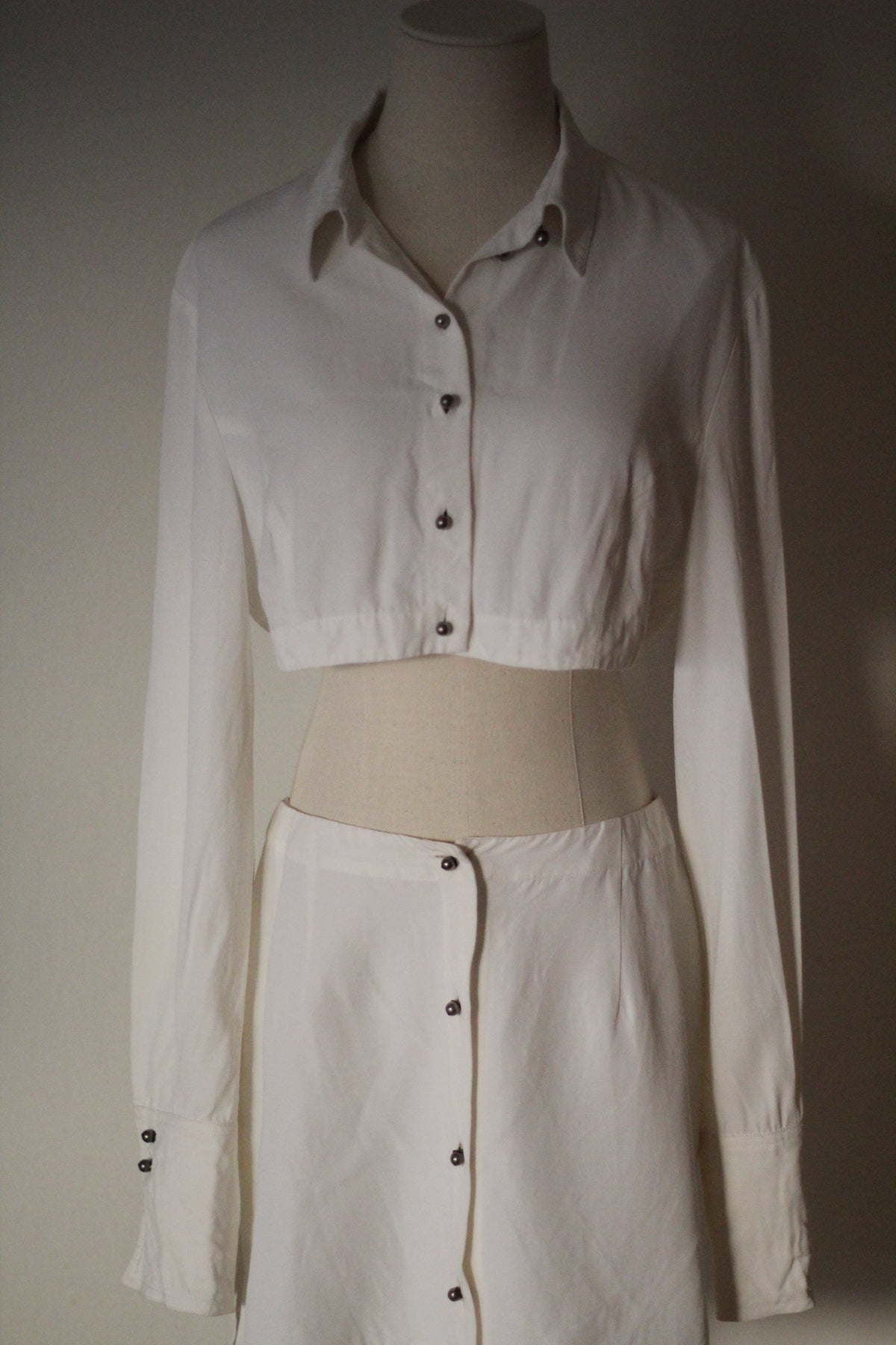 Closer front view of a Rifat Ozbek Spring/Summer 1994 white matching set featuring a cropped button-front shirt and matching button-front mini skirt.